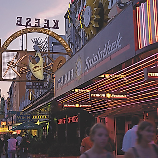 Leuchtende Fassaden und Neonreklame entlang der Reeperbahn bei Abenddämmerung, Passant:innen im Vordergrund