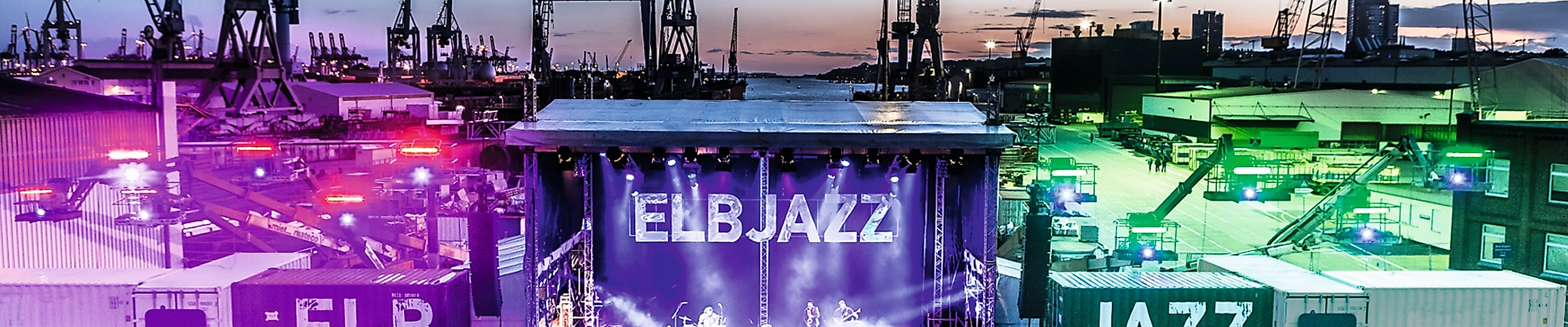 Beleuchtete Bühne des ELBJAZZ Festivals im Hamburger Hafen mit Menschenmenge und Hafenkränen bei Abenddämmerung.