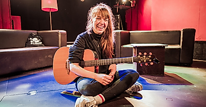 Musikerin mit Gitarre sitzt auf dem Boden des Clubs Molotow, bunte Lichtspots im Raum