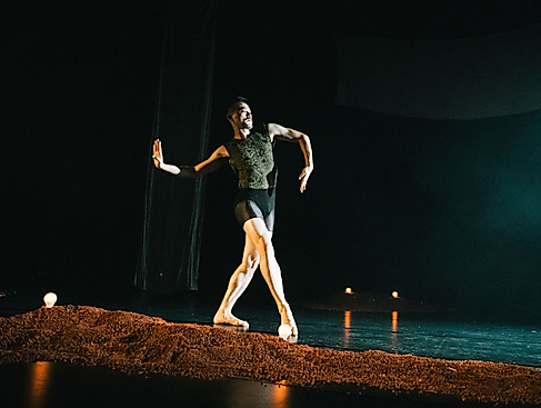 Ausschnitt aus der Tanzproduktion »Choreographing Story »Rama House«« von Chen Wu-kang und Pichet Klunchun. Eine performende Person bewegt sich in einer Ballett-Pose über die Bühne. Vor ihr ist ein kleiner erdartiger Hügel aufgescharrt.