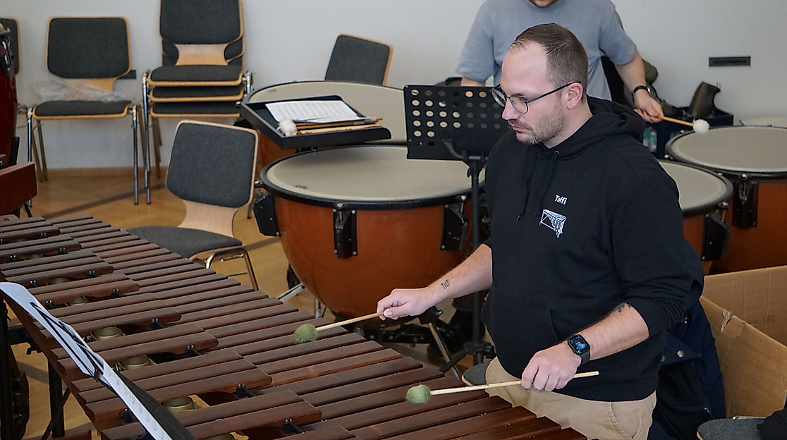 „Rhythmus, der unter die Haut geht: Einblicke in unsere Schlagwerk-Sektion.“

Wenn dieses Instrument erklingt, füllt sich der Saal mit warmer Resonanz. Das Bild zeigt einen unserer Perkussionisten in tiefer Konzentration am Marimbaphon, umgeben von Pauken. Jeder Schlag mit den Schlägeln (Mallets) auf die Holzklangstäbe ist präzises Handwerk und formt den einzigartigen Klangcharakter unseres Orchesters.

Erleben Sie diesen Rhythmus und die klangliche Wucht unseres gesamten Ensembles live und hautnah! Wir laden Sie herzlich zu unserem Konzertabend ein.
