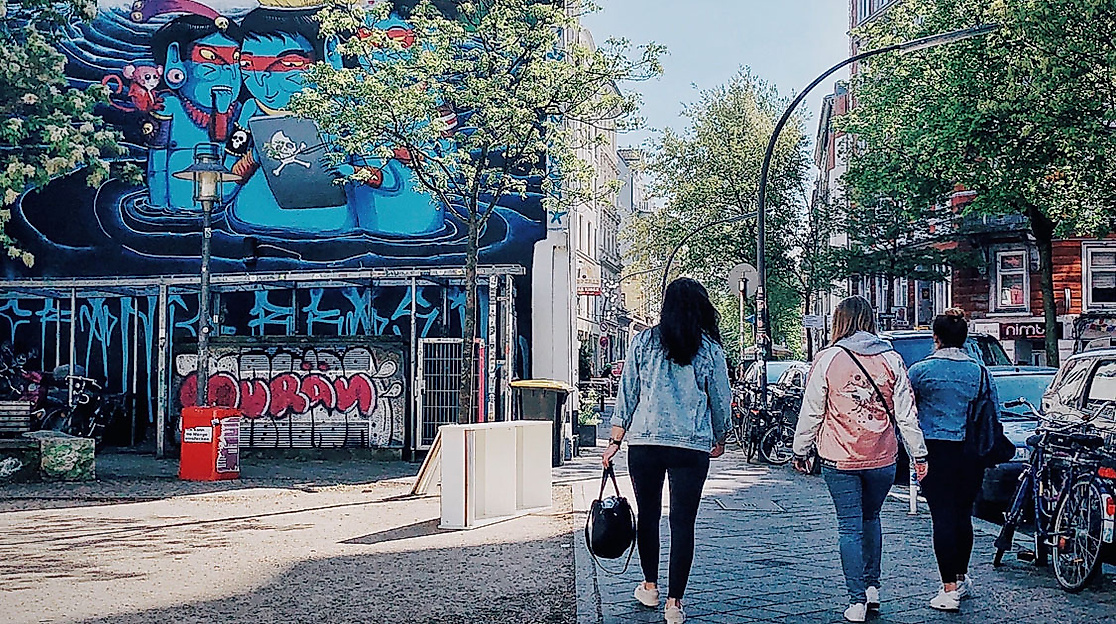Menschen spazieren an bunt bemalter Hausfassade mit Streetart im Schanzenviertel entlang
