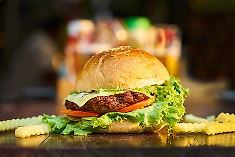 Saftiger Cheeseburger mit Salat und Tomate, serviert mit Pommes auf dunklem Tisch