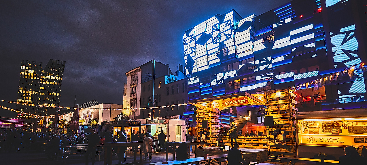 Spielbudenplatz bei Nacht mit beleuchteten Fassaden, Food-Ständen und leuchtender Straßenkunst in Blau und Gelb