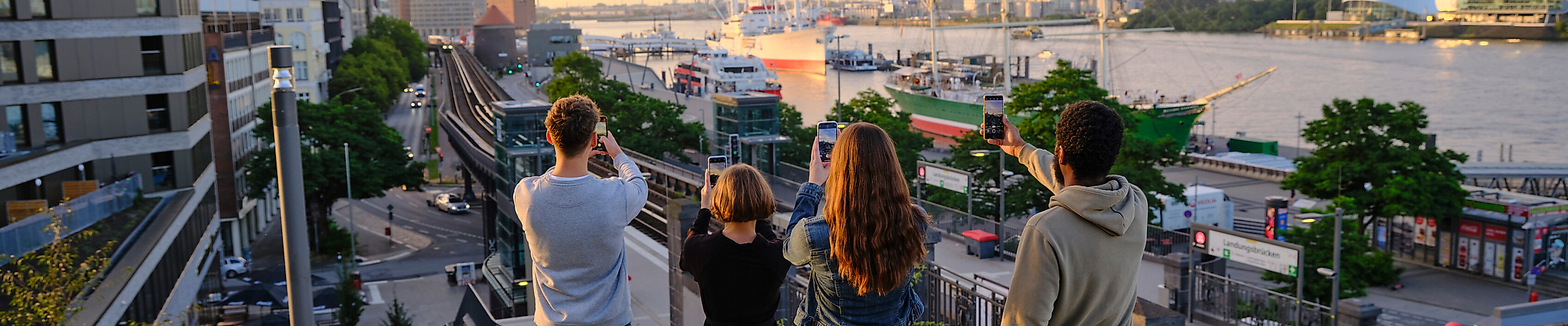 Eine Gruppe junger Erwachsener fotografiert mit ihren Smartphones das Hamburger Panorama.
