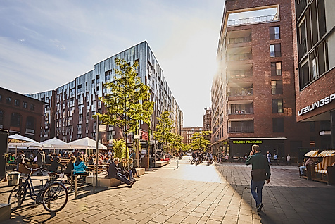 Sonniger Überseeboulevard in der HafenCity Hamburg mit Cafés, modernen Gebäuden und flanierenden Passant:innen