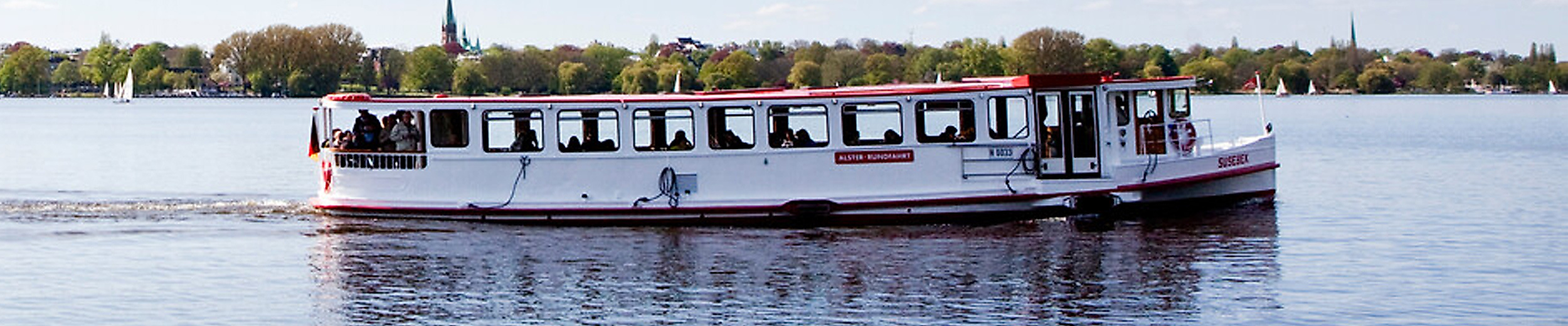 Alsterdampfer mit Passagieren auf ruhigem Wasser vor grüner Uferkulisse in Hamburg