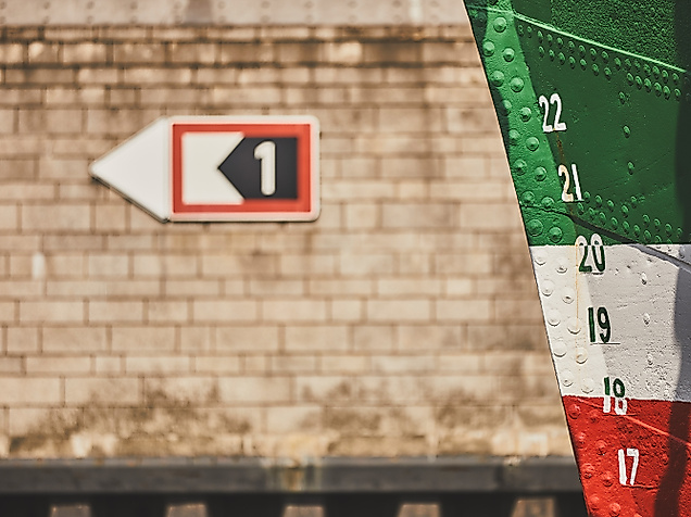 Nahaufnahme des rot-weiß-grünen Bugs der Rickmer Rickmers mit Tiefenmarkierungen vor Kaianlage