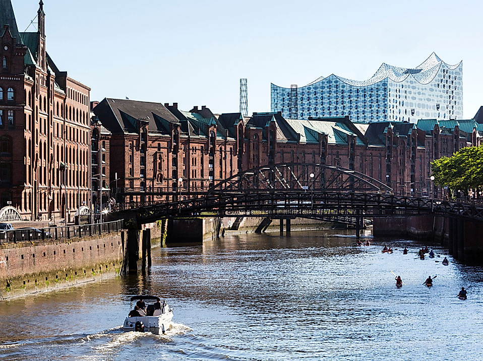 Blick auf Hamburgs Speicherstadt mit Fleetschifffahrt und Elbphilharmonie im Hintergrund bei Tageslicht.