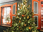 Festlich geschmückter Weihnachtsbaum vor rot gerahmtem Fenster mit warmem Licht und Holzfassade