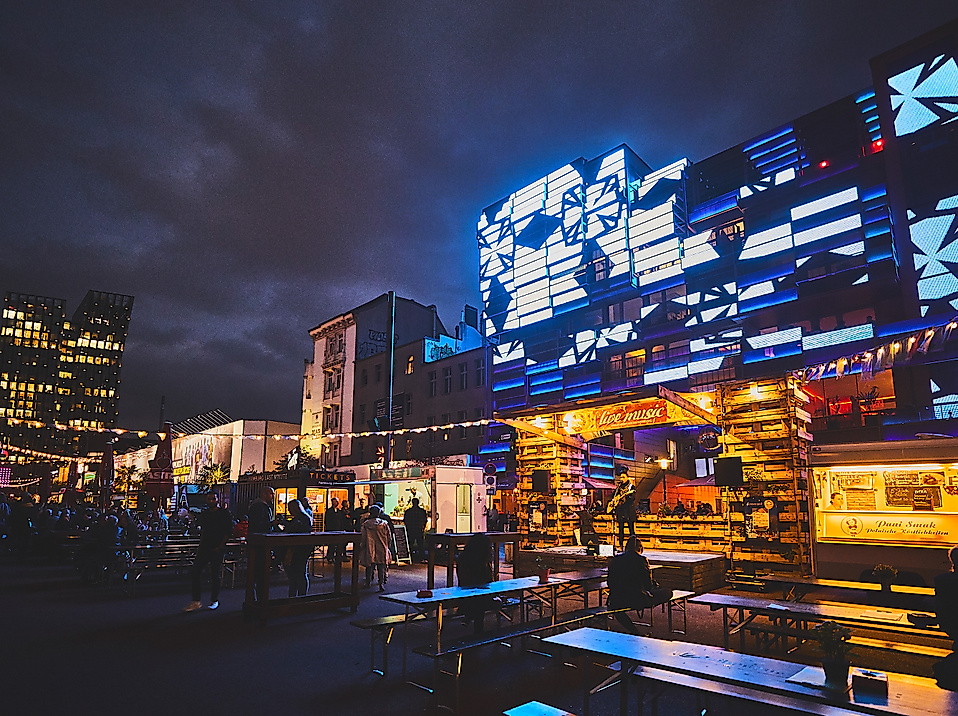 Spielbudenplatz bei Nacht mit beleuchteten Fassaden, Food-Ständen und leuchtender Straßenkunst in Blau und Gelb