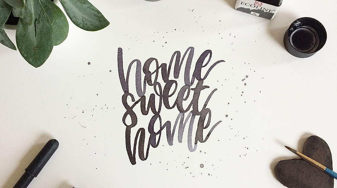 Lettering-Schriftzug „home sweet home“ umgeben von Stiften, Tinte, Deko und Sukkulente auf hellem Untergrund