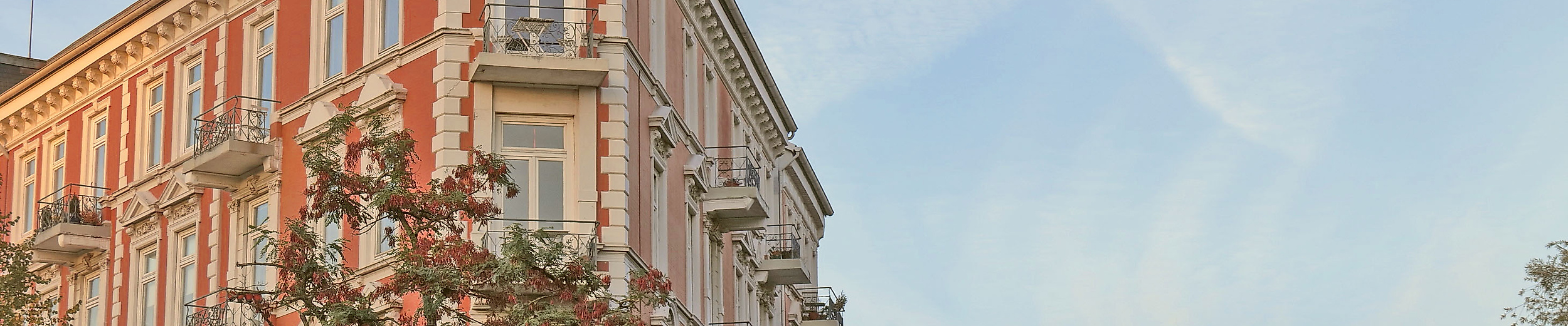 Gründerzeitfassade in Hamburg-Eppendorf im Abendlicht vor herbstlich gefärbten Bäumen und blauem Himmel