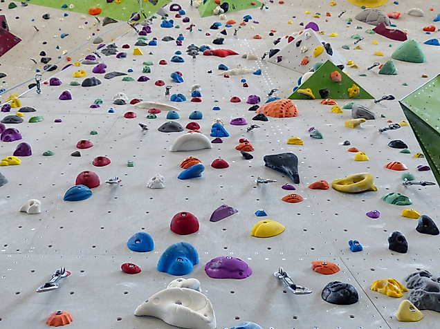Hohe Indoor-Kletterwand mit bunten Griffen und Sicherungsseilen für verschiedene Schwierigkeitsgrade