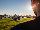 Menschen entspannen im Alsterpark bei Sonnenschein mit Blick auf die Außenalster und die Skyline Hamburgs