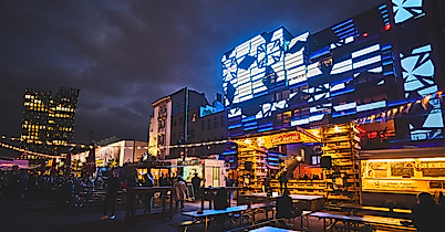 Spielbudenplatz bei Nacht mit beleuchteten Fassaden, Food-Ständen und leuchtender Straßenkunst in Blau und Gelb