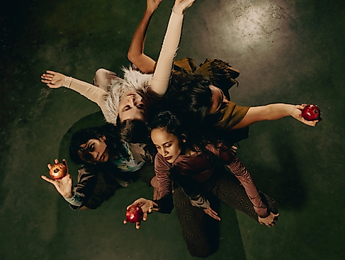 Eine Gruppe Menschen sind eng umschlungen im Kreis. In den Händen halten sie eine Frucht.