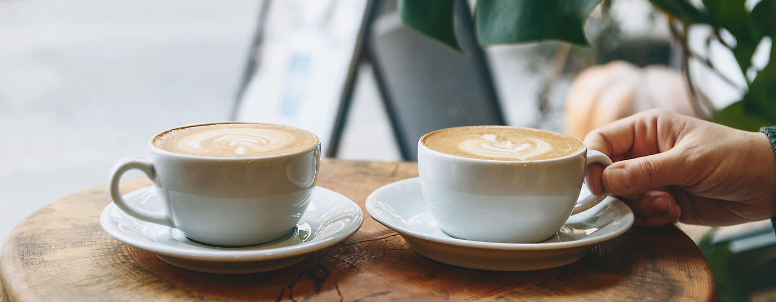 Hand greift Cappucino in Straßencafé