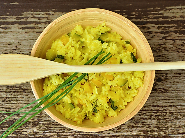 Schüssel mit gelbem Curryreis, garniert mit Schnittlauch, dazu Holzlöffel auf rustikalem Holztisch