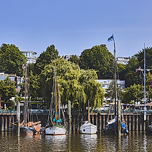 Boote und Masten beim Museumshafen Oevelgoenne in Hamburg, umgeben von Bäumen und sommerlichem Wetter