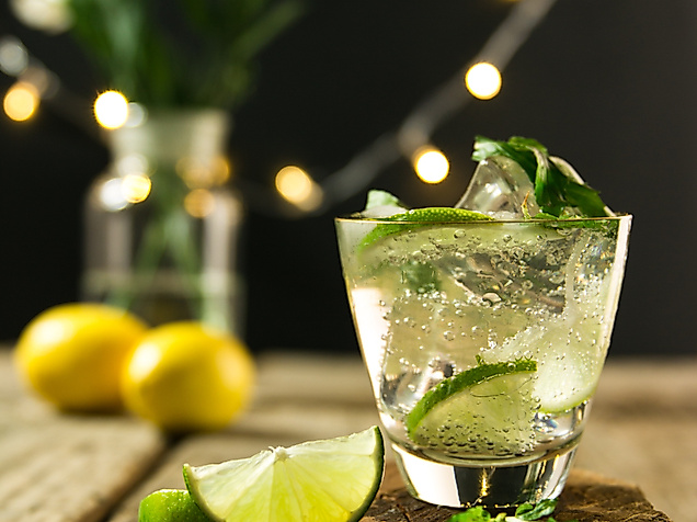 Erfrischender Cocktail mit Limette und Minze auf Holztisch, stimmungsvolle Lichter im Hintergrund