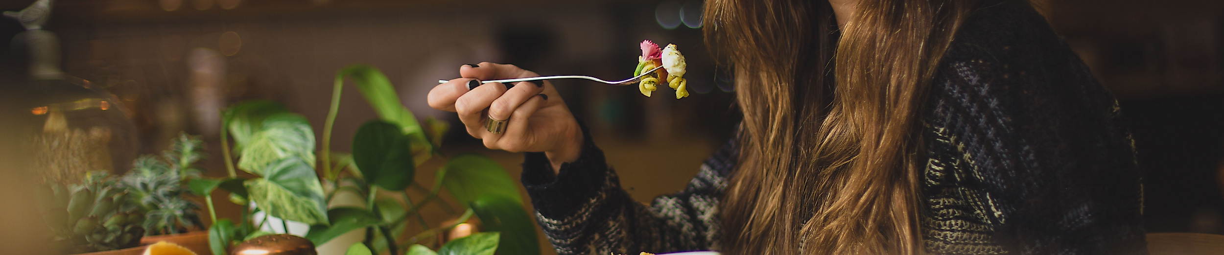 Frau genießt entspannt ein Gericht in stilvoll beleuchtetem Restaurantambiente mit Pflanzen-Deko