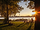 Sonnenuntergang im Alsterpark mit Blick durch Bäume auf entspannte Menschen an der Außenalster