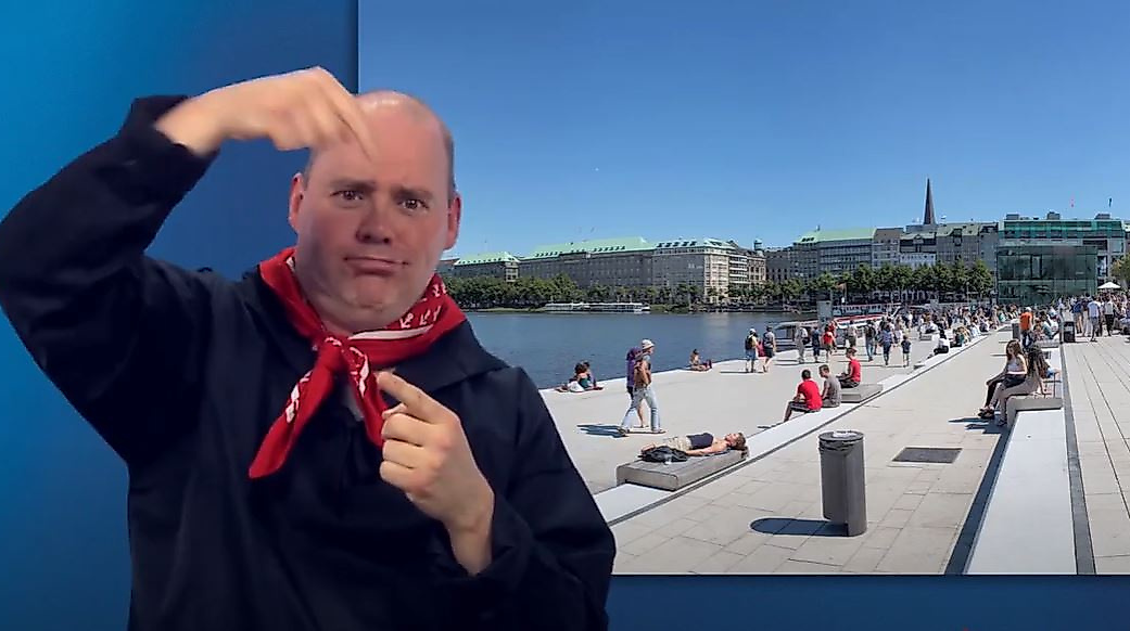 Mann gebärdet vor sonniger Alsterpromenade mit vielen Menschen – barrierefreie Informationen zur Alster in Hamburg.