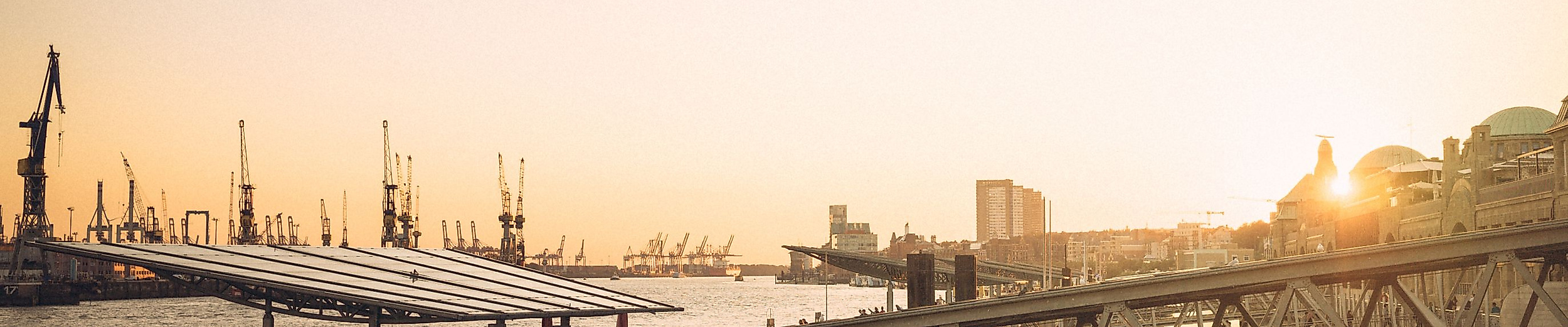 Sonnenuntergang an den Landungsbrücken mit Blick auf Elbe, Schiffe und historische Gebäude im Gegenlicht