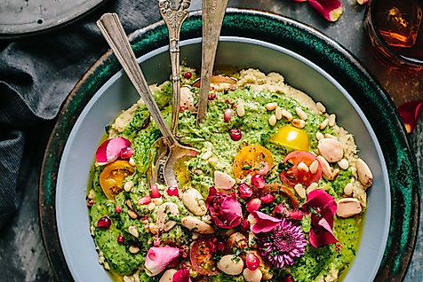 Farbenfrohe vegetarische Bowl mit Gemüse, Kräutern und essbaren Blüten, stilvoll angerichtet mit Besteck
