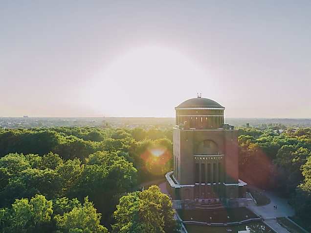 Planetarium Hamburg im Wasserturm des Stadtparks bei Sonnenaufgang über grünem Blätterdach