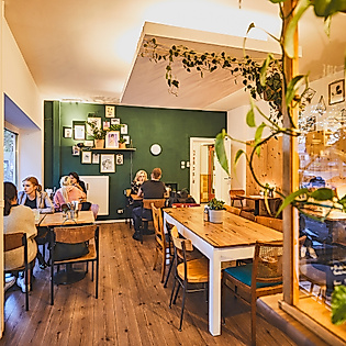 Modernes, gemütlich bepflanztes Café Happenpappen mit Holzboden, großen Tischen und grüner Wandgestaltung