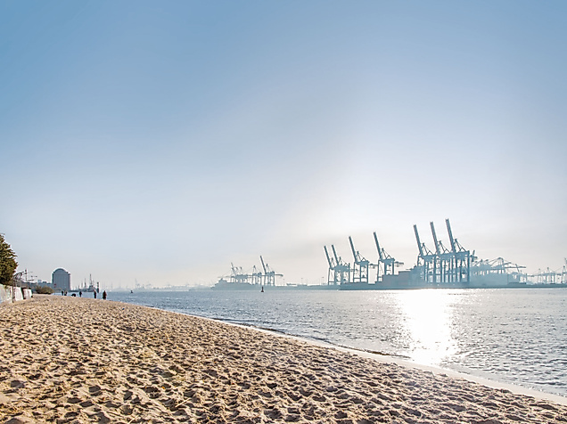 Sonniger Elbstrand mit Blick auf Containerkräne im Hamburger Hafen und glitzerndem Wasser