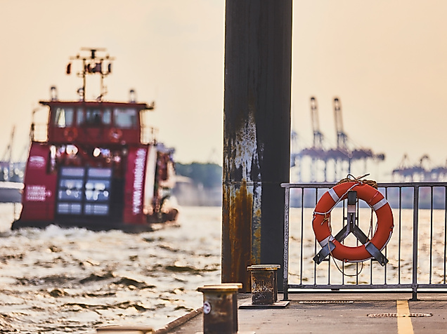 HADAG-Fähre im Hamburger Hafen, aufgenommen vom Anleger mit Rettungsring und Containerkränen im Hintergrund