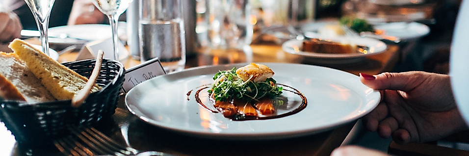 Fein gedeckter Restauranttisch mit Wein und stilvoll angerichtetem Hauptgericht in geselliger Runde