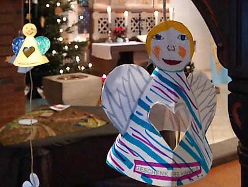 selbstgebastelte Engel hängen von der Empore; im Hintergrund ist der Altar zu sehen