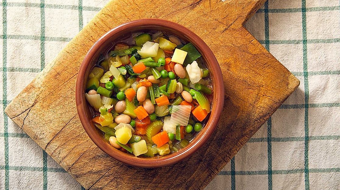 Schale mit bunter Gemüsesuppe aus Erbsen, Karotten und Kartoffeln auf Holzbrett und Küchentuch