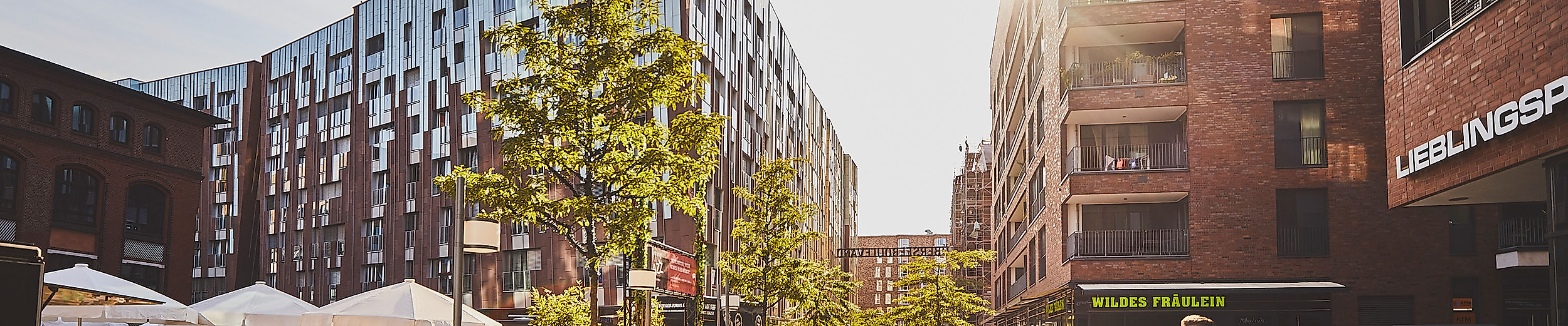 Sonniger Überseeboulevard in der HafenCity Hamburg mit Cafés, modernen Gebäuden und flanierenden Passant:innen