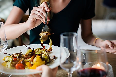 Person genießt buntes Gemüsegericht bei Kerzenschein und Rotwein in stilvollem Restaurant