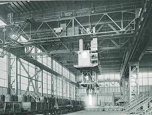 Ein altes schwarz-weiß Foto der ehemaligen Fabrikhallen von Kampnagel mit Gerüsten, einem Kran und aufgereihten Metall-Tonnen.