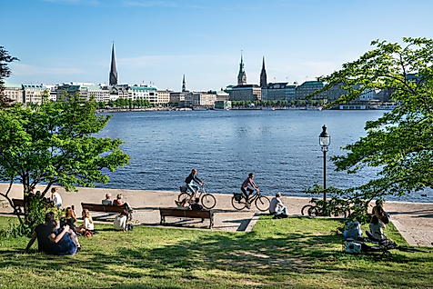 Menschen entspannen und radeln im Sommer an der Binnenalster mit Blick auf Hamburgs Skyline